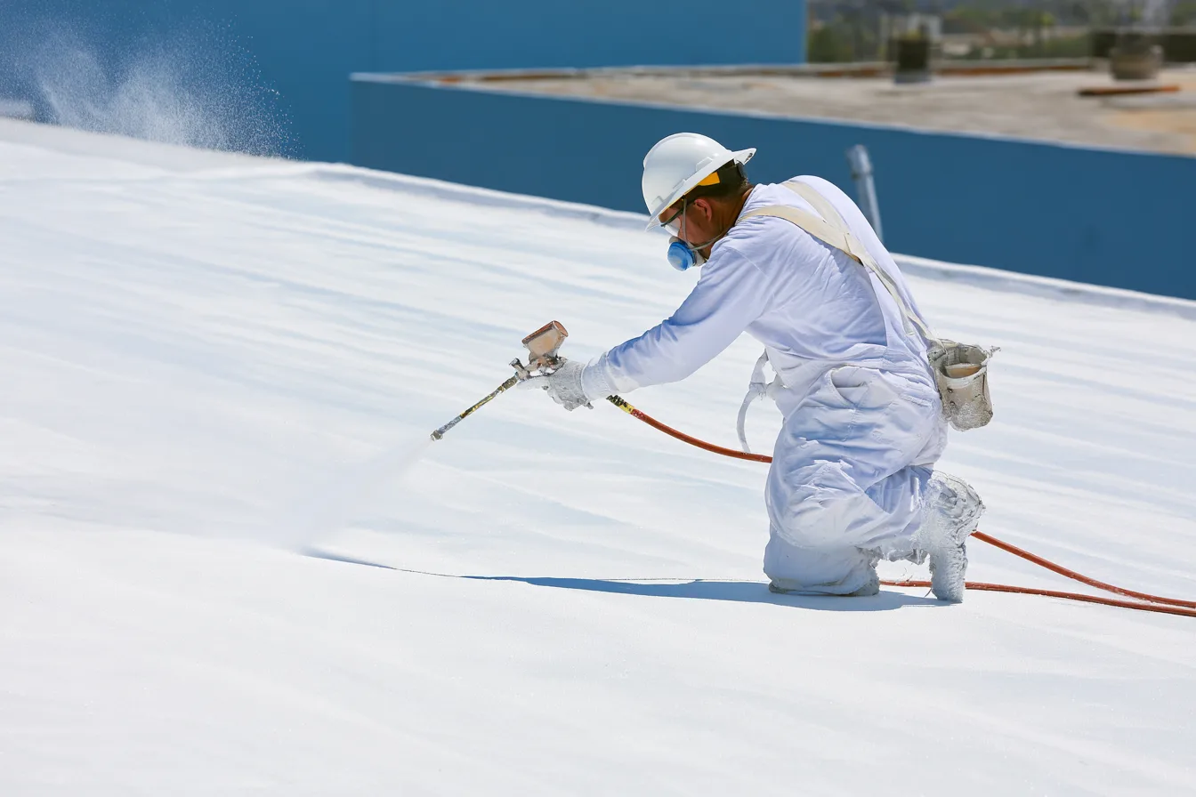 Worker in protective gear spray coating a white commercial roof
