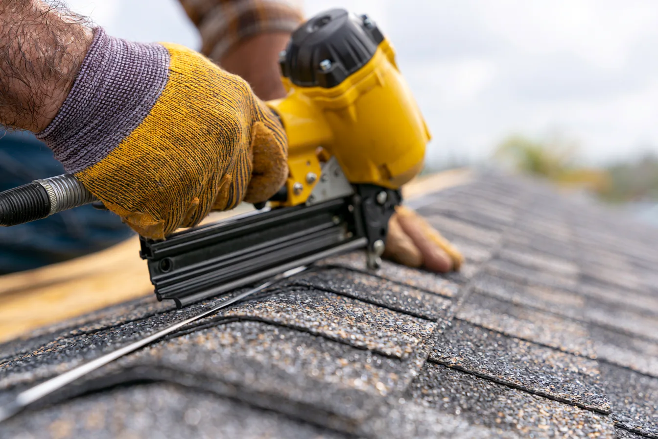 Gloved hands nailing fresh ridge cap shingles